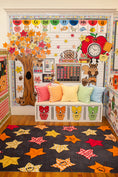 Load image into Gallery viewer, A cozy autumn-themed children's room corner featuring a white bench with owl face carvings, colorful gingham pillows, a large paper tree, a fall alphabet chart, and a dark rug with colorful maple leaves.