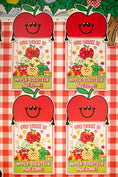 Load image into Gallery viewer, Four identical apple-themed classroom reward cards arranged in a 2x2 grid on a red and white gingham checkered tablecloth. The cards feature a large smiling red apple at the top, with the text 'OUR WORK IS APPLE-SOLITELY AWESOME!' and a colorful illustration of apples and fruit.