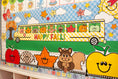 Load image into Gallery viewer, A colorful autumn-themed classroom wall display featuring a yellow school bus with 'HAPPY FALL!' text, smiling apples, a leaf, a squirrel, clouds, stars, and a blue-and-white checkered sky.