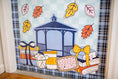 Load image into Gallery viewer, A decorative autumn-themed window decal or sticker sheet featuring a blue gazebo, gift boxes with bows, books, a coffee cup, a pastry, and scattered fall leaves on a light blue check background.
