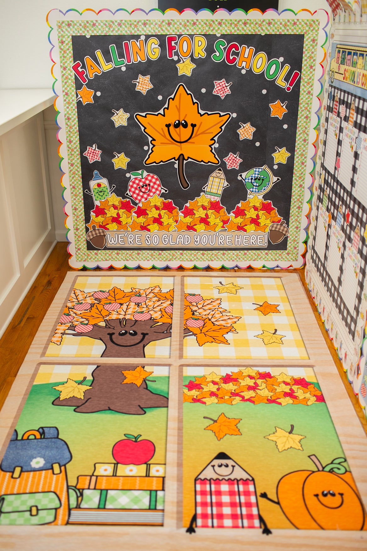 A handmade autumn-themed classroom display board and matching floor mats in a school classroom. The display features a large backboard with 'FALLING FOR SCHOOL!' and a smiling maple leaf, plus four matching floor mats below with school and fall motifs.