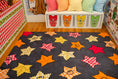 Load image into Gallery viewer, A dark gray area rug with a playful pattern of colorful autumn maple leaves in red, orange, yellow, and white, styled in a children's room with a matching white storage bench and gingham pillows.

