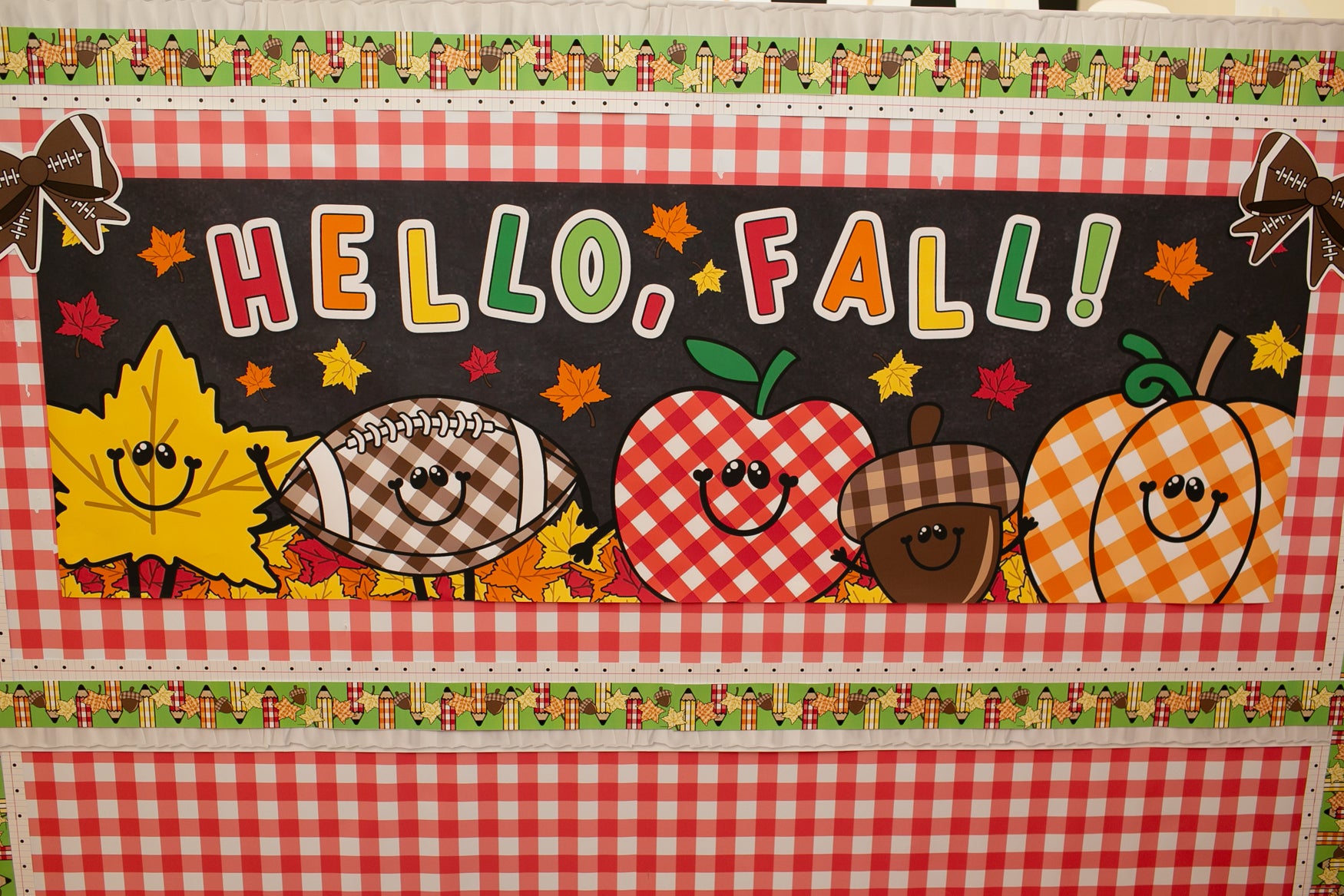 hello fall in primary colors walgreens classroom horizontal banner with a pumpkin, acorn, acorn, pumpkin, football and leaf on it with gingham details on a black background. 
