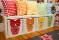 Load image into Gallery viewer, A white storage bench with four drawers decorated with colorful apple faces and bows, topped with six gingham throw pillows in red, orange, yellow, green, and blue, set in a child's room.
