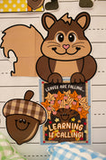 Load image into Gallery viewer, A fall-themed paper craft or decoration featuring a cartoon squirrel, an acorn, and a small autumn message card that reads 'LEAVES ARE FALLING.
