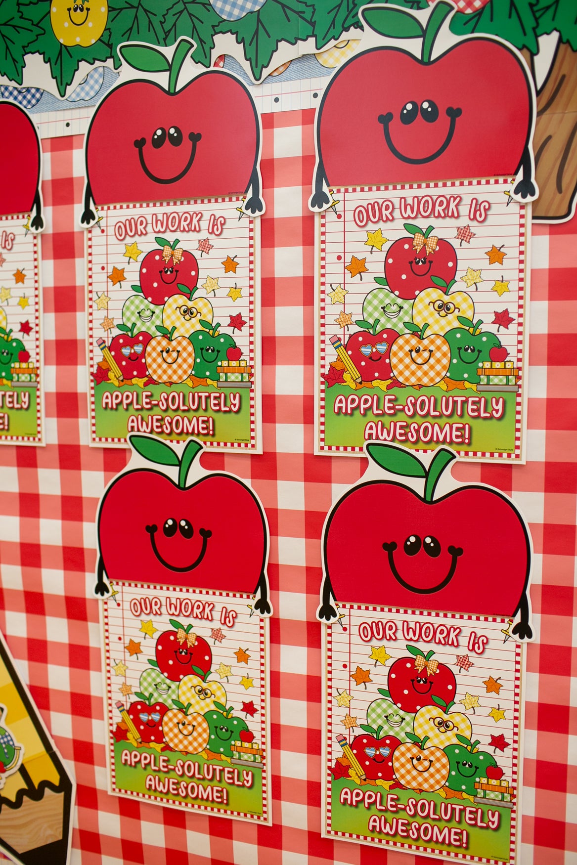 A close-up of a red and white checkered surface with repeated printed apple-themed labels that read 'OUR WORK IS APPLE-SOLITELY AWESOME!' and 'APPLE-SOLITELY AWESOME!'. The labels feature smiling red apples and fruit illustrations.