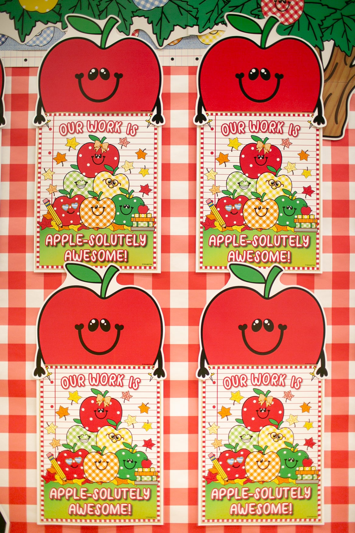 Four identical apple-themed classroom reward cards arranged in a 2x2 grid on a red and white gingham checkered tablecloth. The cards feature a large smiling red apple at the top, with the text 'OUR WORK IS APPLE-SOLITELY AWESOME!' and a colorful illustration of apples and fruit.