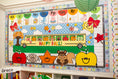 Load image into Gallery viewer, A colorful children's educational wall display with autumn-themed graphics, including a school bus, apples, leaves, a squirrel, clouds, and alphabet letters, mounted on a wall above a shelf.
