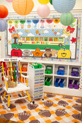 Load image into Gallery viewer, A colorful children's classroom corner with a fall-themed educational board, storage bins, a white rocking chair, and an acorn-patterned floor. Paper lanterns hang from the ceiling.
