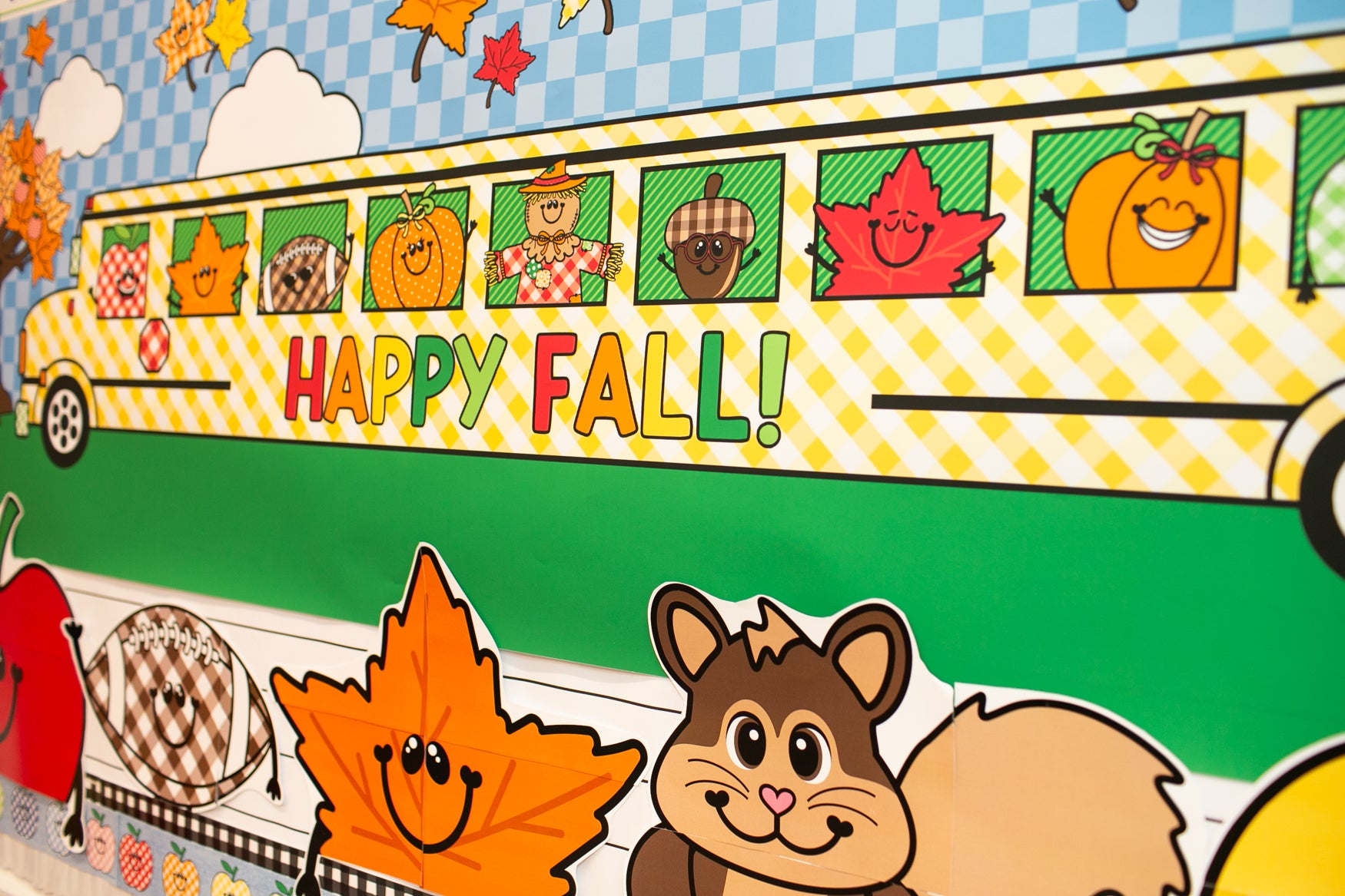 horizontal happy fall classroom banner that you get printed at Walgreens and the bus has happy fall icons peeking out of the window such as a leaf, scarecrow, acorn, and gingham apples.  