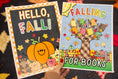 Load image into Gallery viewer, Two autumn-themed bookish posters held up by a hand. The left poster says 'HELLO, FALL!' with a pumpkin, stars, and fall colors.
