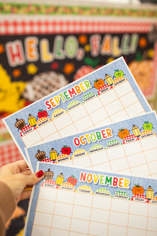 Three printable monthly planner pages for September, October, and November are held up by a hand with red nail polish. The pages feature a blue denim-style border and colorful autumn-themed illustrations of pumpkins, apples, and fall gear.